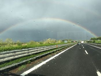Rainbow over road against sky