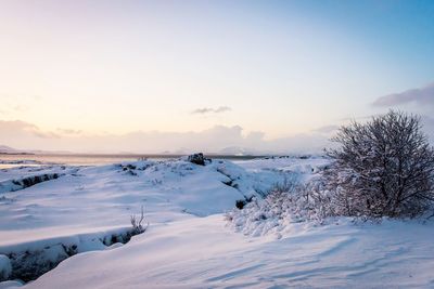 Snow covered landscape against sky during sunset