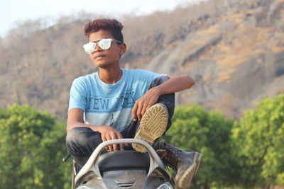 Full length of teenage boy sitting against mountain on motor scooter