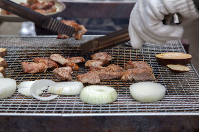 Cropped image of person cooking meat and onion on barbecue grill