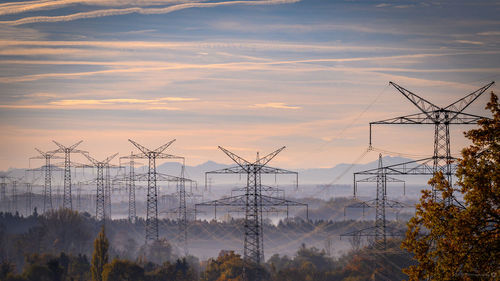 Electricity pylons against sky during sunset