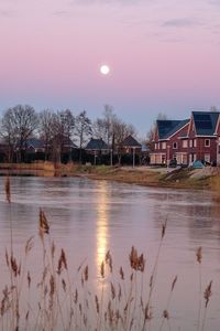 Houses by lake and buildings against sky at sunset