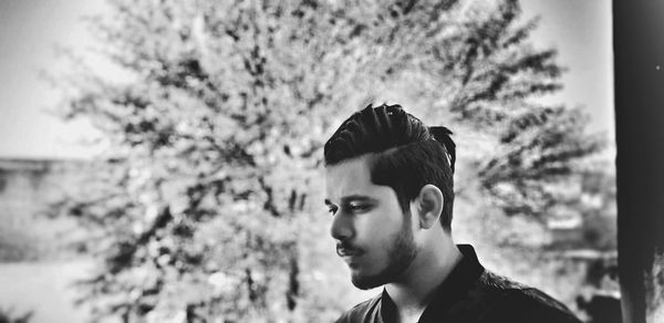 Portrait of young man looking away against trees