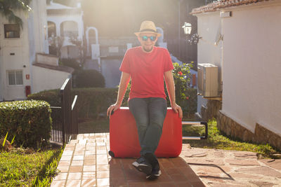 Full length portrait of man sitting on footpath against building