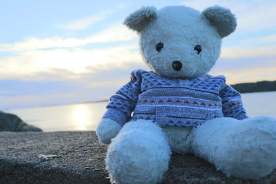 Full length of boy sitting on rock at sea shore against sky