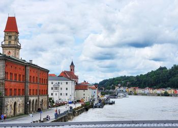 Buildings by river against cloudy sky