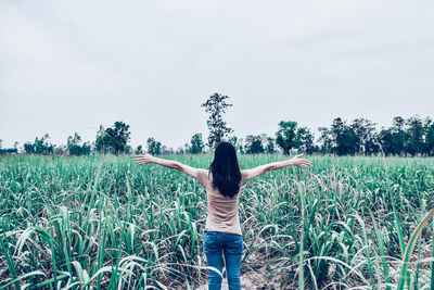 Rear view of woman standing with arms outstretched on field against sky