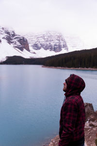 Man standing by lake against snowcapped mountains