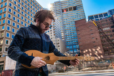 Low angle view of man playing guitar against buildings in city