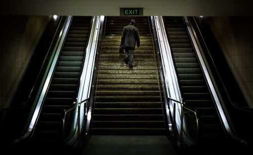 Rear view of man walking on steps by escalator in subway station
