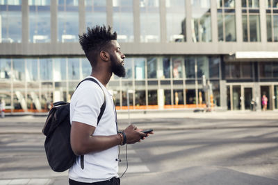 Side view of young man holding smart phone while in city