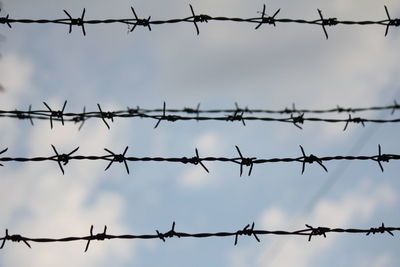 Close-up of barbed wire fence against sky