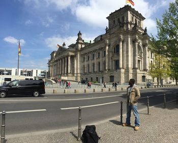 Man standing on sidewalk in city against sky