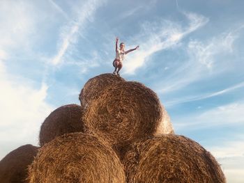 Low angle view of woman crouching on hay bale against sky