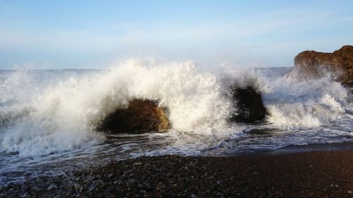 Waves splashing on shore against sky