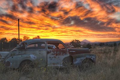 Abandoned car on field during sunset