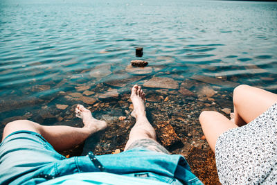 Low section of couple sitting at lakeshore