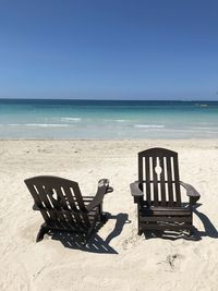 Empty chairs on beach against clear sky