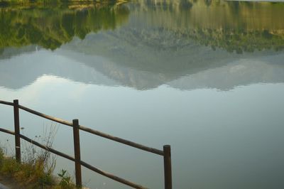 Reflection of railing in lake against sky