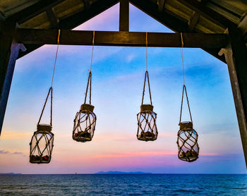 Low angle view of lanterns hanging over sea against sky during sunset