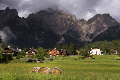 Houses on field by dolomites against cloudy sky