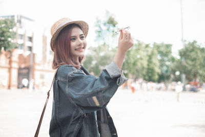 Portrait of smiling young woman standing against city in background