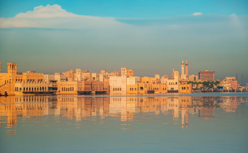 Buildings by river against sky during sunset