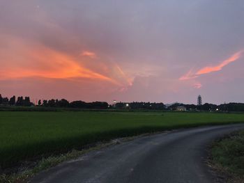 Road amidst field against sky during sunset