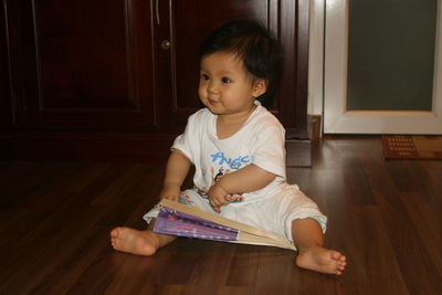 Cute girl looking away while sitting on hardwood floor