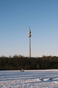 Tower on snow covered land against clear blue sky