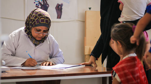 Nurse writing on paper at clinic with patients