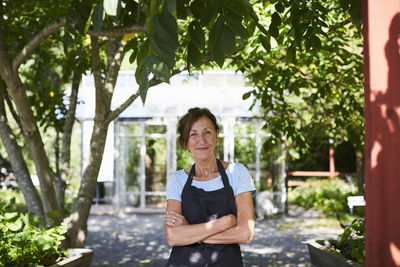 Portrait of confident female gardener standing arms crossed at yard