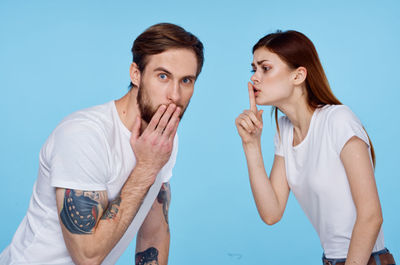 Woman gesturing with man against blue background