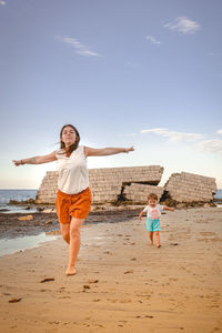 Full length of mother and daughter on beach against sky