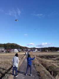 People flying over field against sky