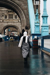 Rear view of woman walking on bridge against buildings in city