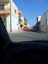 Cars on road by buildings against blue sky