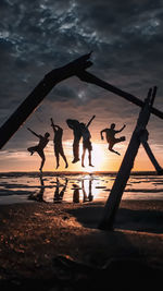 Silhouette people on beach against sky during sunset