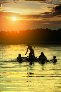 Silhouette people in sea against sky during sunset