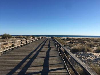Boardwalk leading towards landscape against clear blue sky
