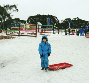 Full length of boy standing with sled on snow covered field