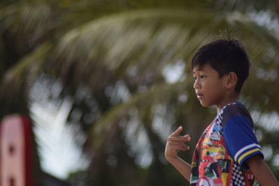 Side view of cute boy standing against palm trees