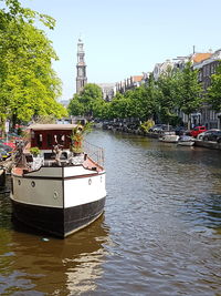 Sailboats moored on river by buildings against sky