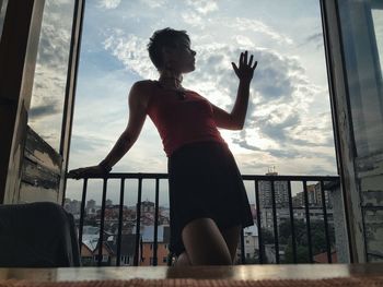 Full length of woman standing by railing against sky seen through window