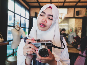 Young woman wearing hijab while holding camera in store