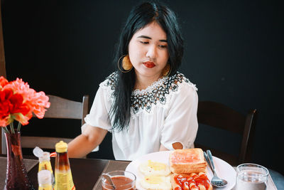 Woman with breakfast on table sitting against black background