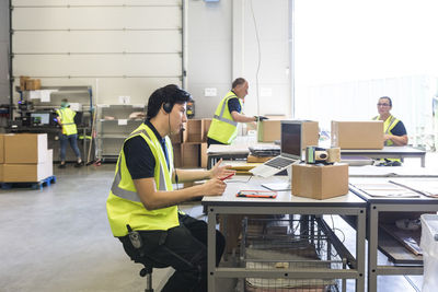 Young customer service representative talking through headset while coworkers at warehouse