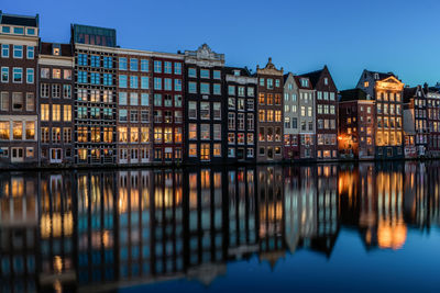 Reflection of illuminated row houses on canal at dusk