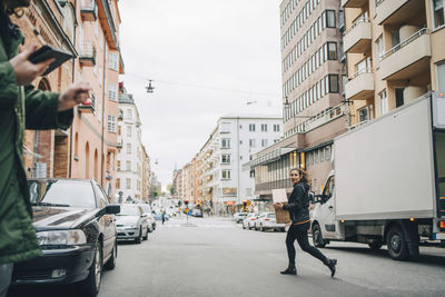 Woman running by delivery van while carrying box in city against clear sky