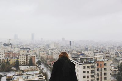 Rear view of woman looking at cityscape against sky